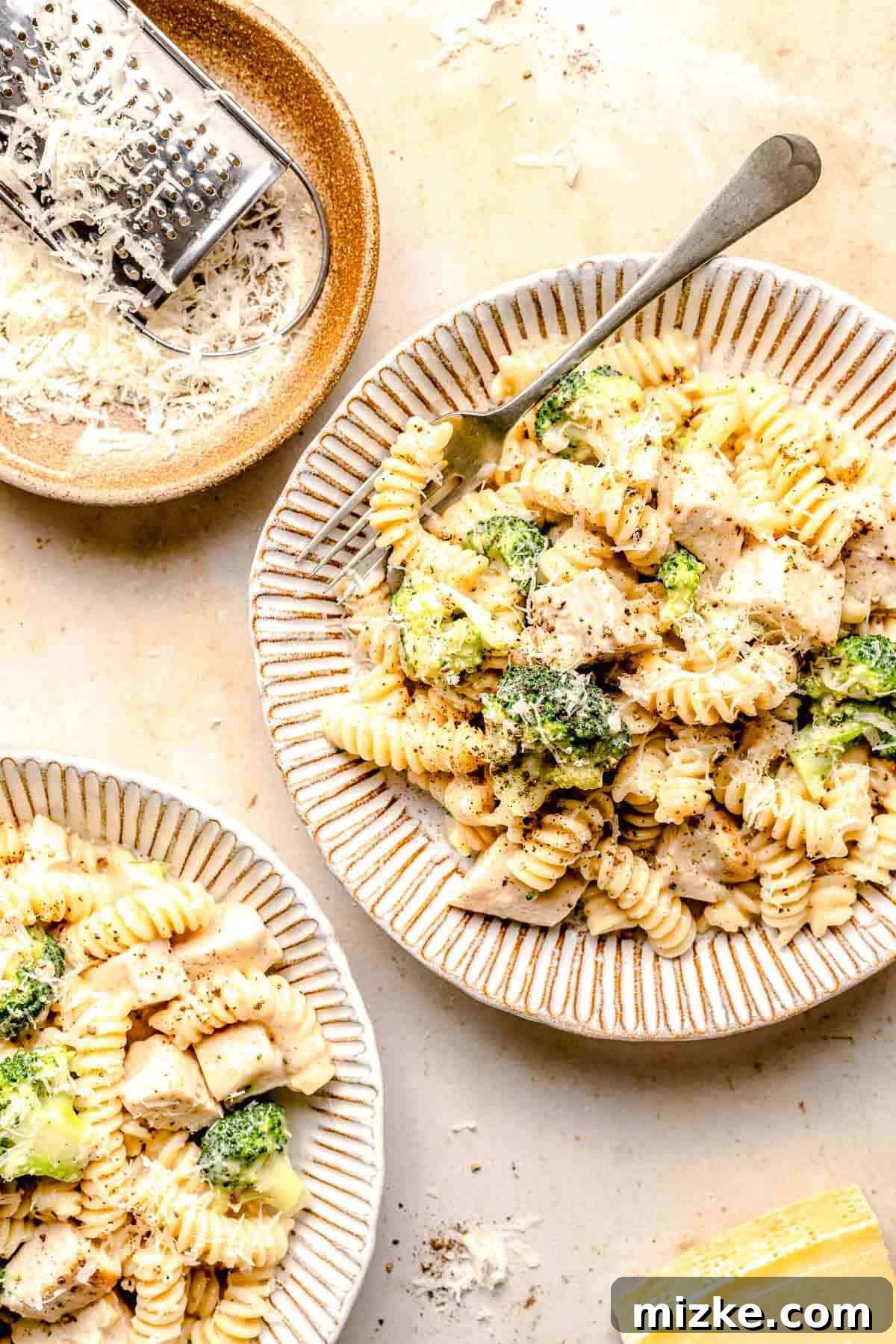 Close-up of a serving of Chicken Broccoli Alfredo pasta, ready to eat. A vibrant bowl of Chicken Broccoli Alfredo pasta, garnished with fresh basil leaves and a generous sprinkle of Parmesan cheese. The creamy sauce glistens, highlighting the tender chicken and broccoli.