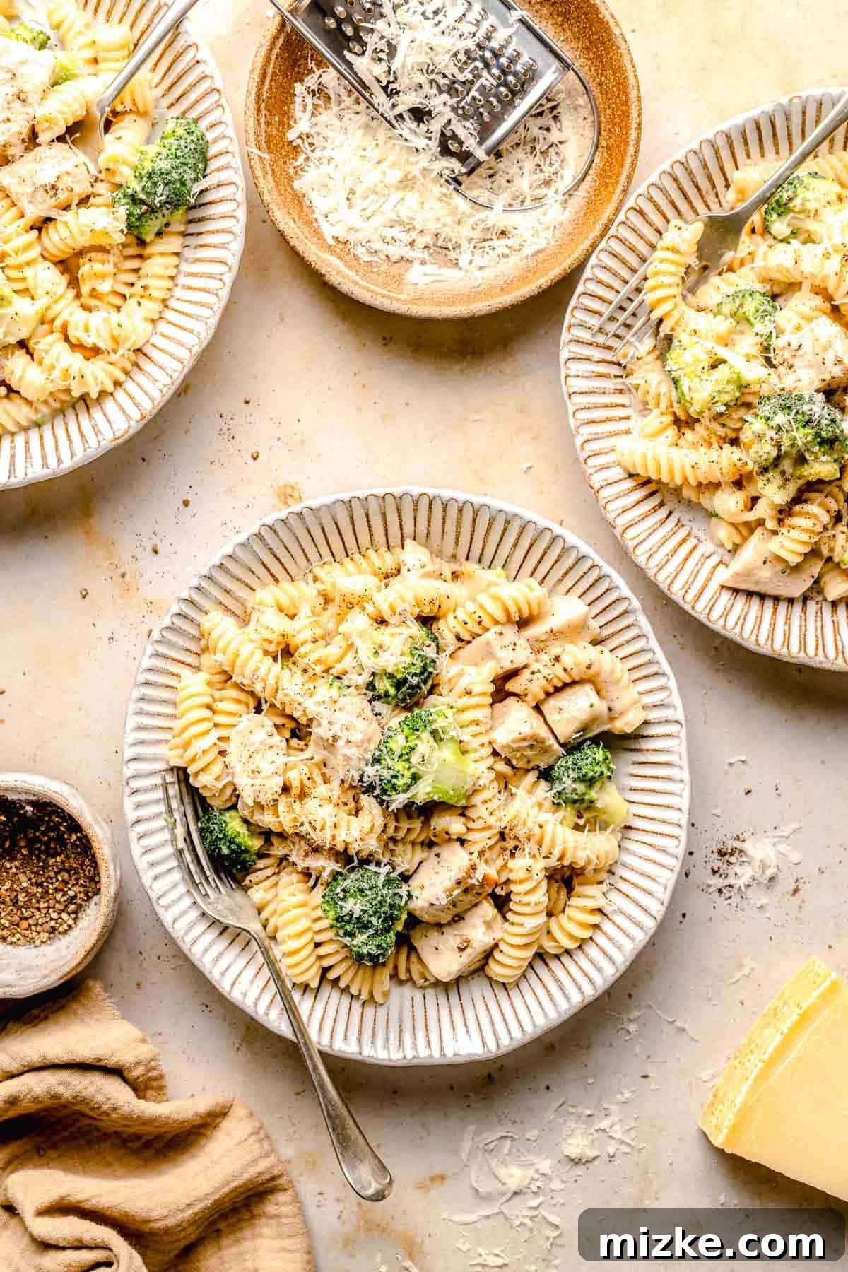 Family-style serving of Chicken Broccoli Alfredo pasta in multiple bowls. Several bowls of Chicken Broccoli Alfredo pasta beautifully arranged on a rustic wooden table, ready for a family meal.