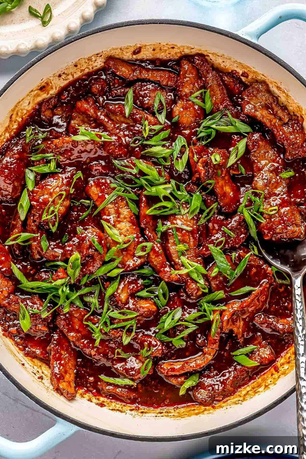 Sweet and Savory Mongolian Beef 2 A pan of cooked beef strips in rich sauce, garnished with chopped green onions.