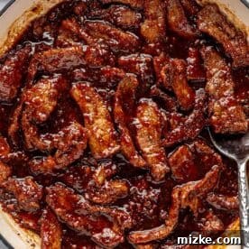 Sweet and Savory Mongolian Beef 12 A pot filled with strips of beef coated in a rich, dark sauce. A spoon rests on the edge of the pot.