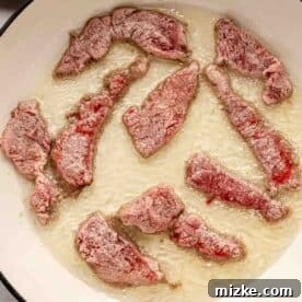 Sweet and Savory Mongolian Beef 10 Slices of beef frying in oil in a round black skillet.