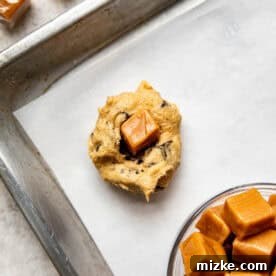 cookie dough on a parchment lined baking sheet with a soft caramel in the center of the dough