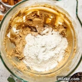 flour being added to the wet mixture in a glass stand mixer bowl