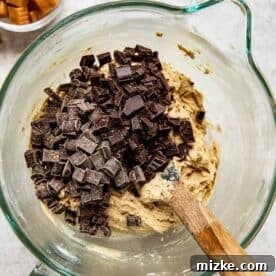 chocolate chunks added into the cookie dough in a glass stand mixer bowl