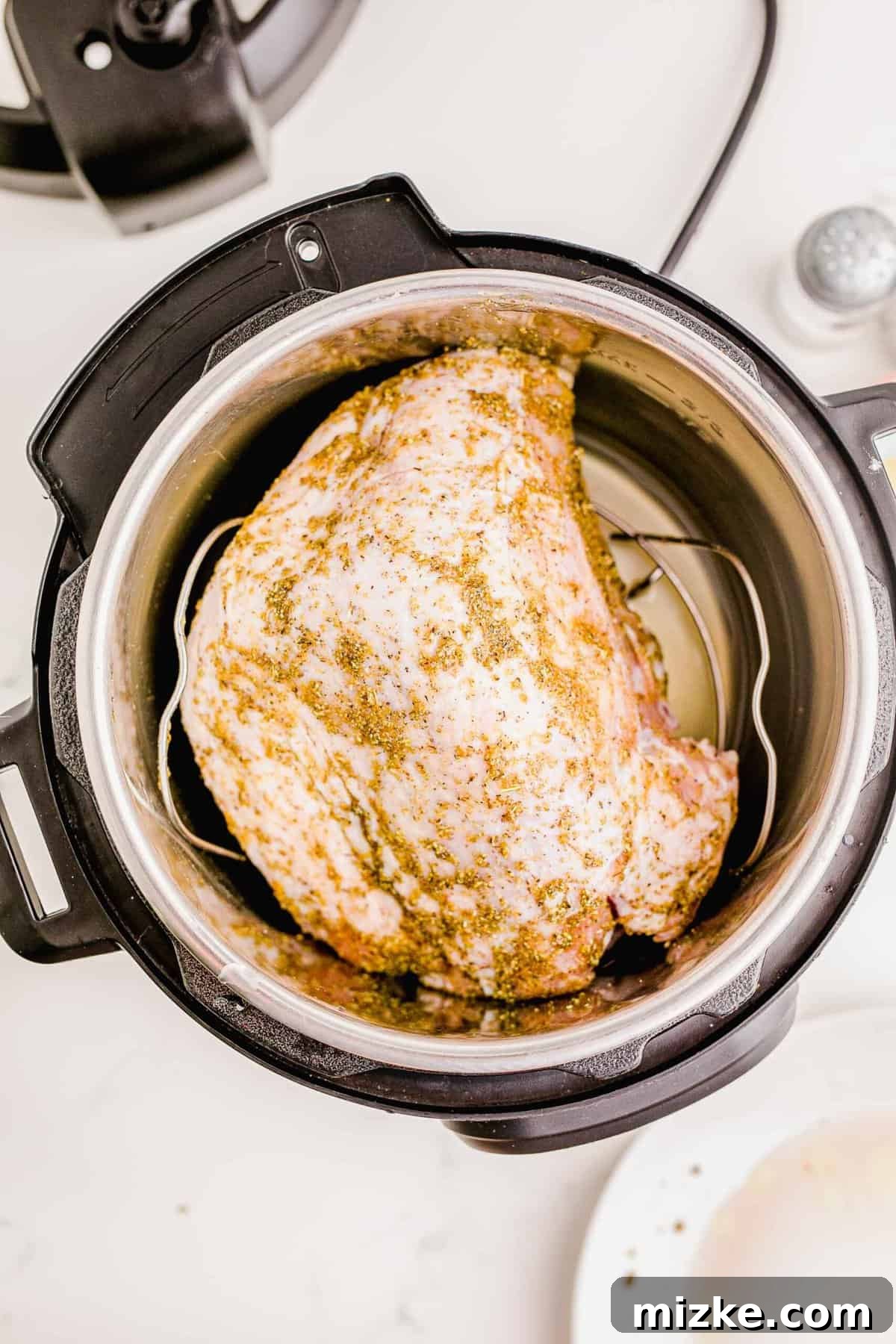 Perfect Instant Pot Turkey Breast 8 Placing a seasoned turkey breast on a metal trivet inside the Instant Pot with chicken broth, ready for pressure cooking.