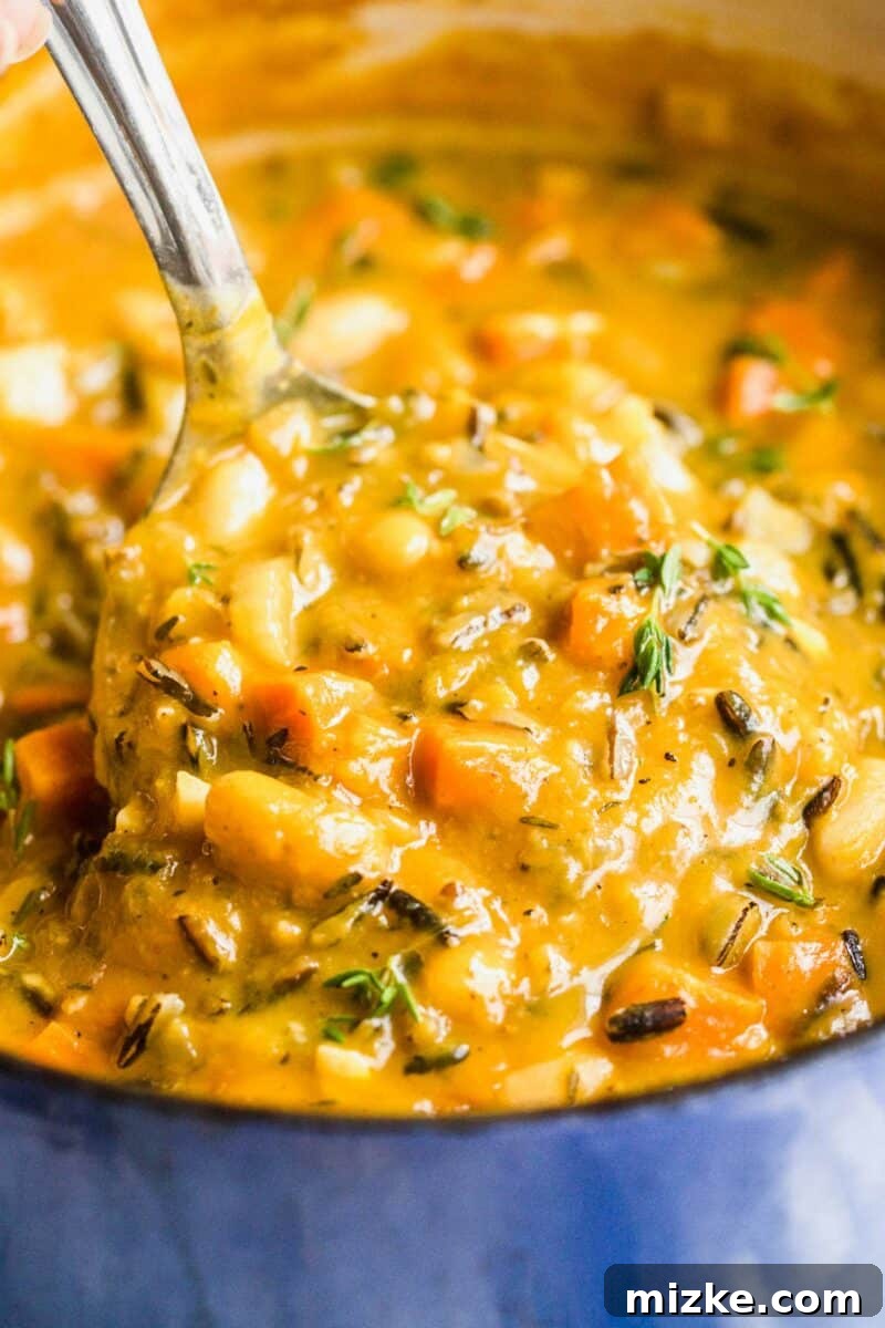 Golden Vegan Pumpkin Wild Rice Harvest Bowl 2 A spoon is lifting a bite sized portion of nourishing pumpkin wild rice soup from a blue bowl, garnished with fresh herbs.