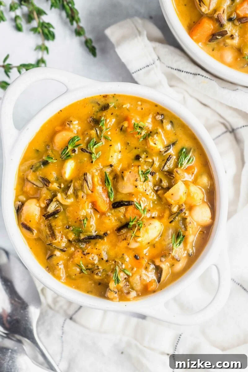 Golden Vegan Pumpkin Wild Rice Harvest Bowl 3 Fresh thyme and sage leaves garnish a full white bowl of nourishing pumpkin wild rice soup.