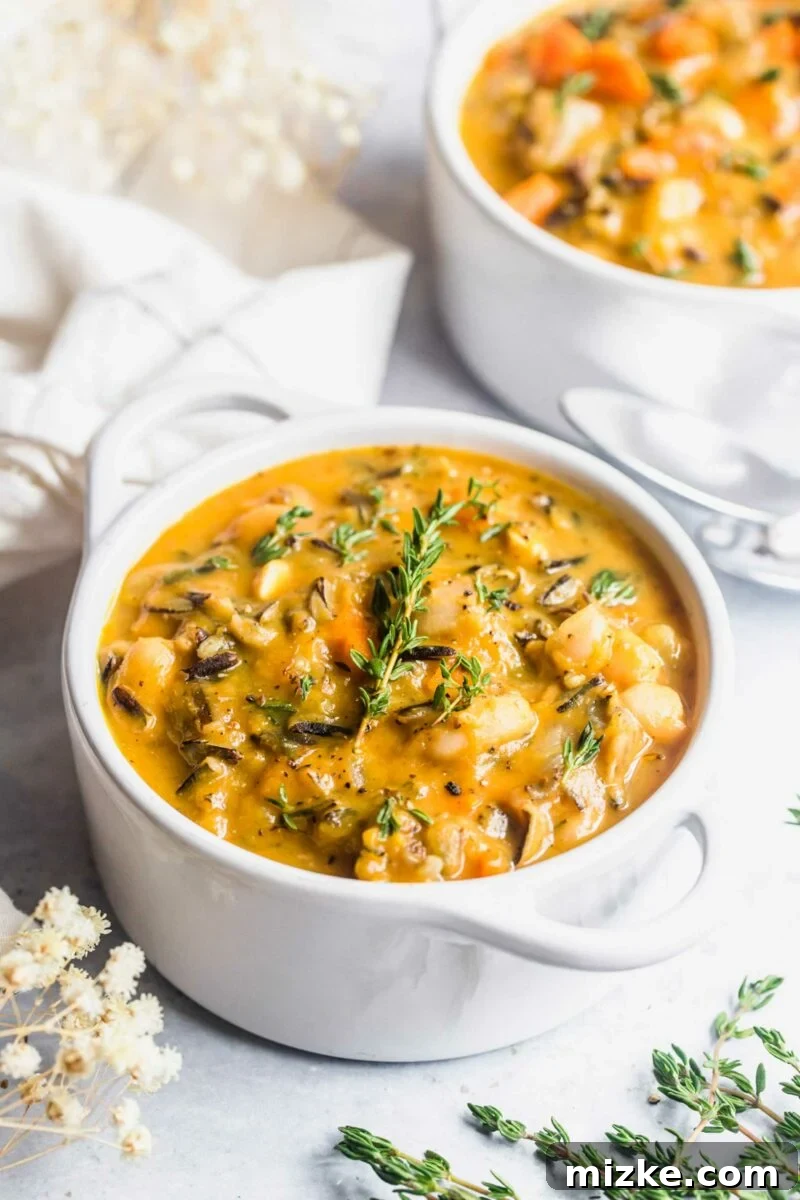 Golden Vegan Pumpkin Wild Rice Harvest Bowl 4 A large white pot is filled to the brim with steaming pumpkin wild rice soup and is garnished with fresh thyme.