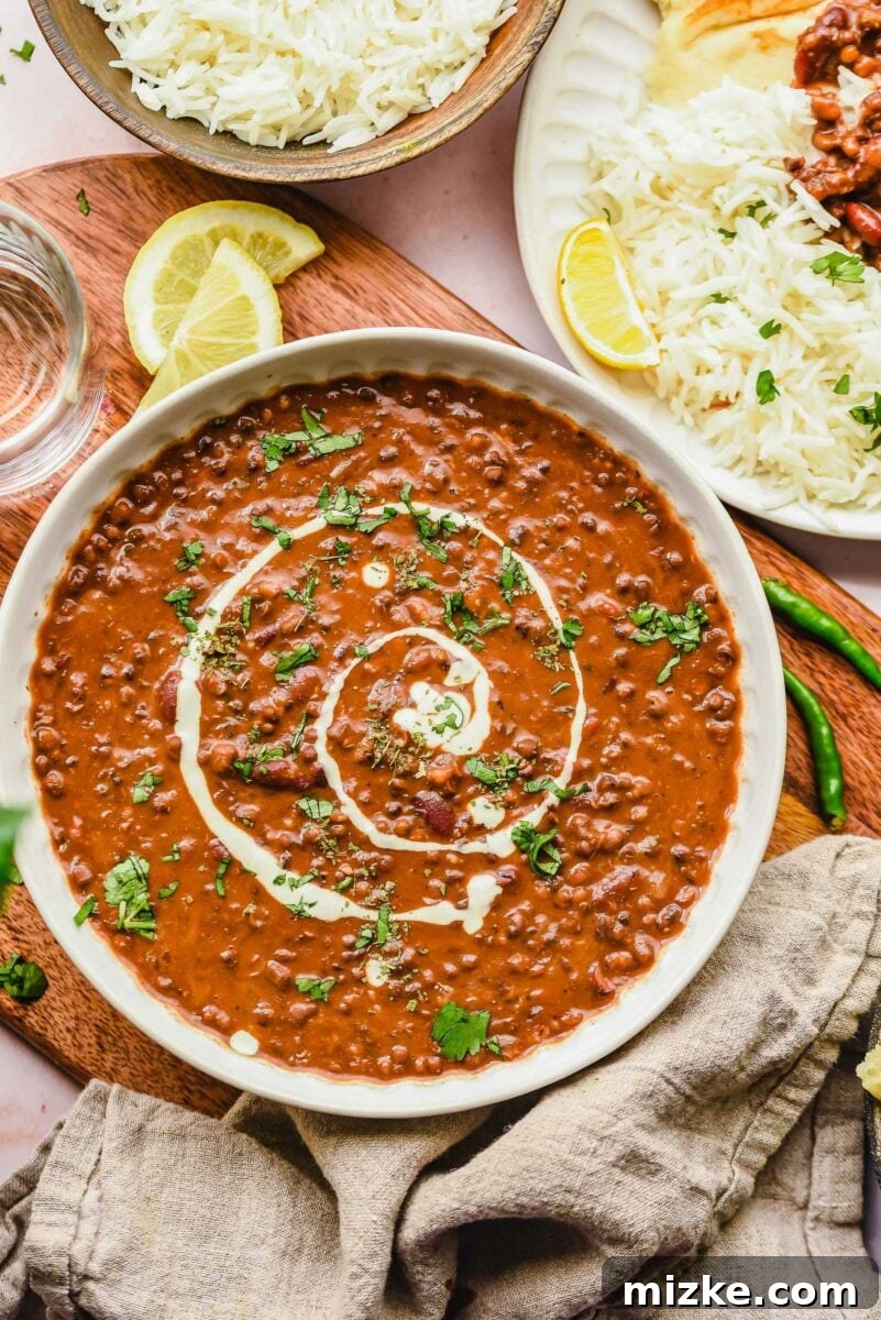 A bowl of dal makhani is presented on a wooden surface next to a beige linen tea cloth.