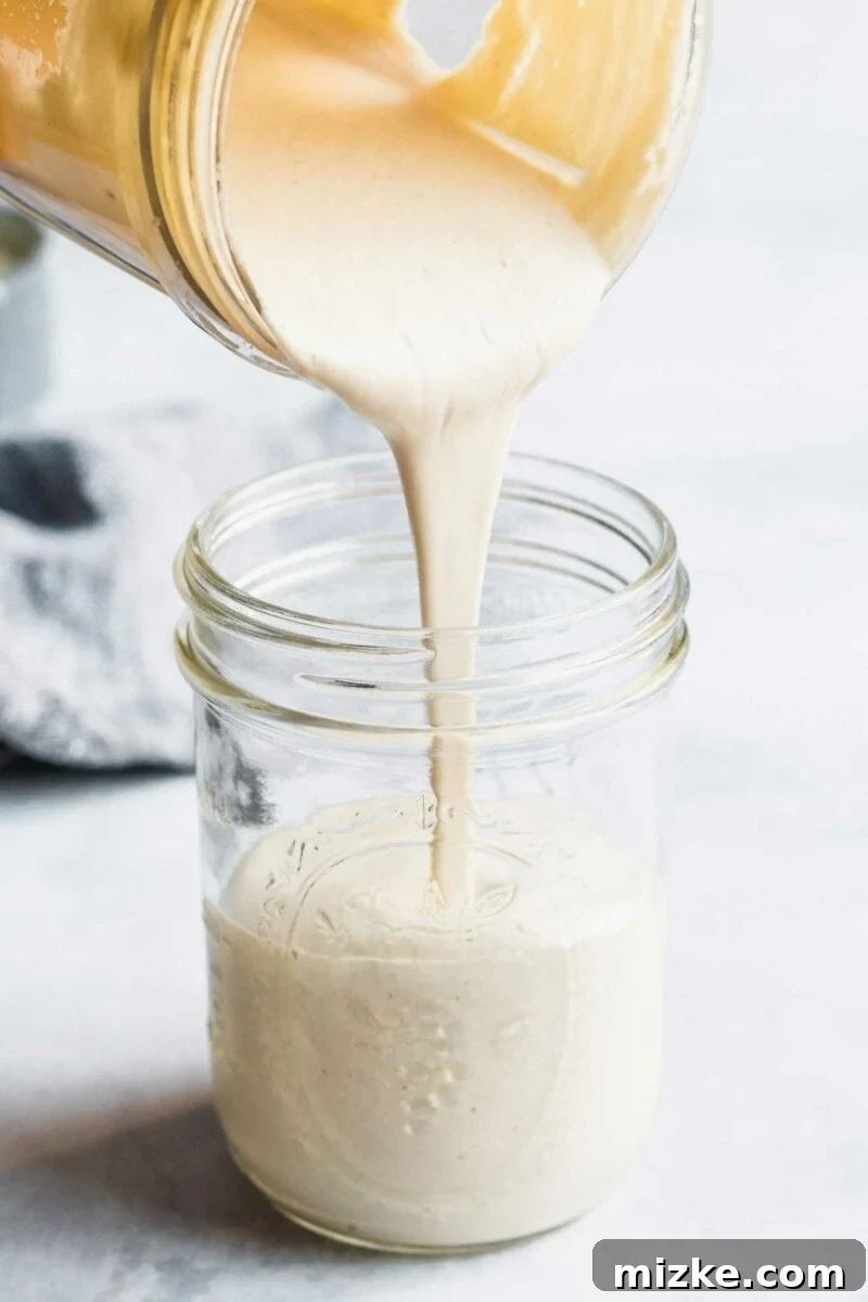Dreamy Vegan Cashew Cream 2 Smooth vegan cashew cream sauce being poured from a blender into a clear glass jar.