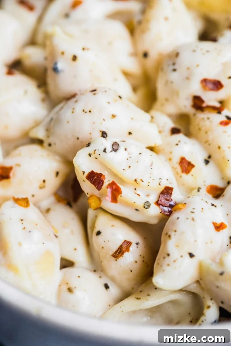 Velvety Vegan Pasta Shells 5 Red pepper flakes and cracked black pepper are artfully sprinkled across a serving of creamy vegan pasta shells, enhancing its visual appeal and promising a delightful culinary experience.