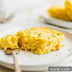 A slice of cornbread casserole on a plate with a bite taken out of it.
