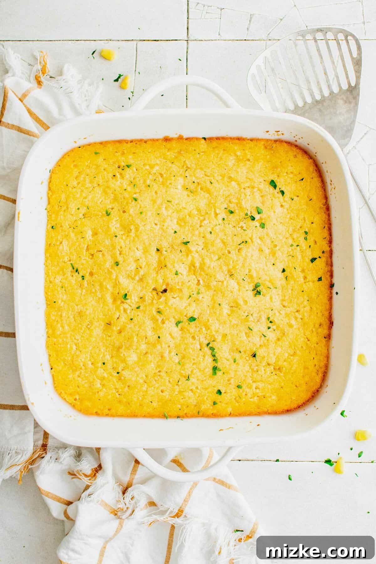 This Jiffy cornbread casserole bakes to a beautiful golden brown, promising a perfect side dish for any meal. An inviting overhead view of a golden-baked corn casserole, nestled perfectly in a rustic baking dish, fresh out of the oven.