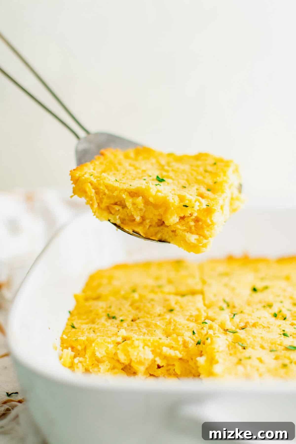 This Jiffy cornbread casserole is easy to make and serves perfectly, making it a favorite for gatherings. A spatula carefully lifts a warm, golden slice of cornbread casserole from the baking dish, steam gently rising.