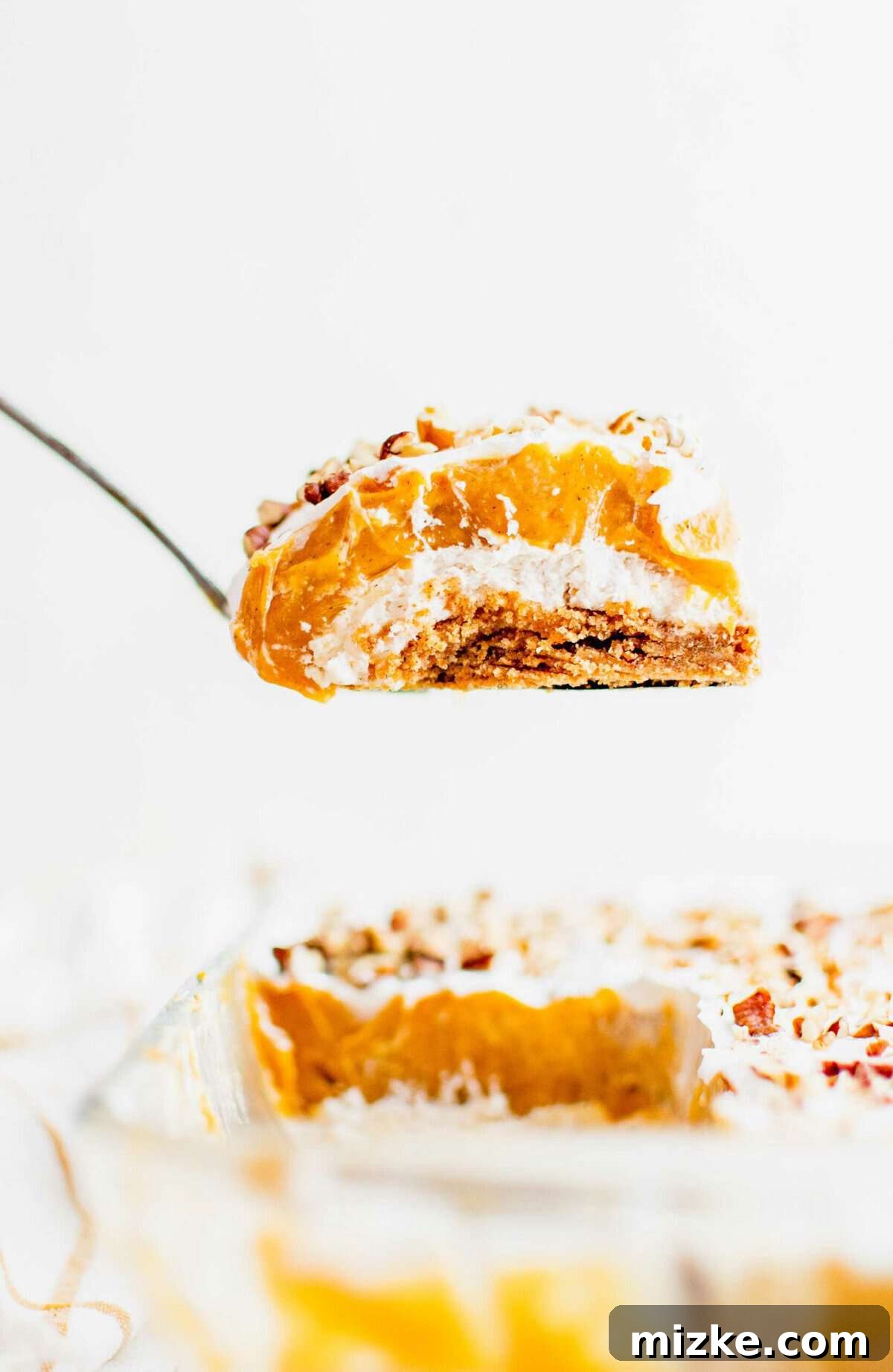Pumpkin Delight: A layered fall dessert with cream cheese, pumpkin, whipped cream, and cookie crust. A small serving of pumpkin lush is being lifted from the baking dish, showcasing its distinct layers.