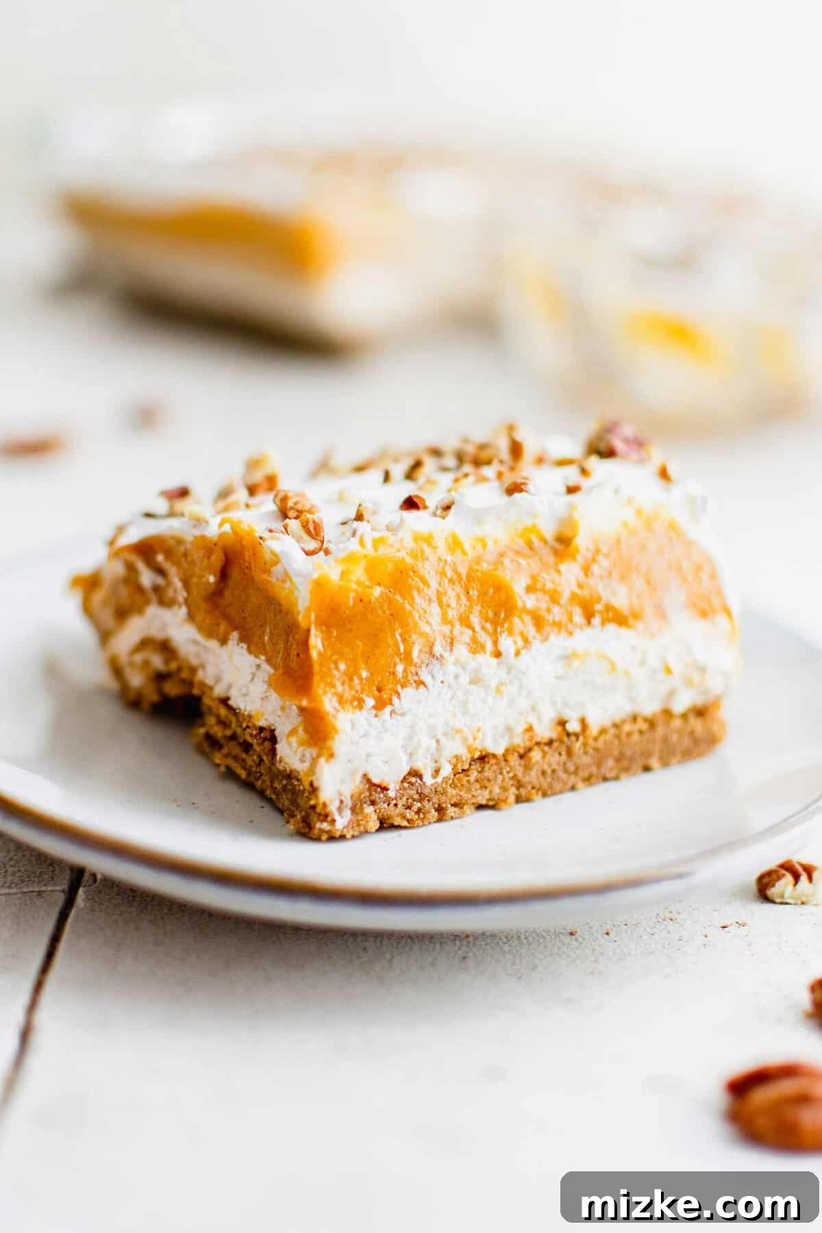 A perfect slice of Pumpkin Delight, showcasing its beautiful layers. A layered slice of pumpkin delight is presented on a white plate.