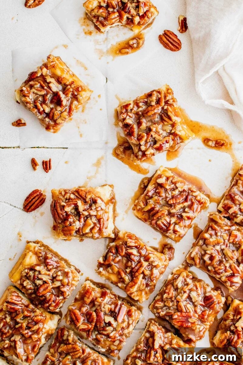 Decadent Pecan Pie Cheesecake Bars 2 Several pecan pie cheesecake bars are sliced and presented on a white surface, showcasing their distinct layers of crust, creamy cheesecake, and rich pecan topping.