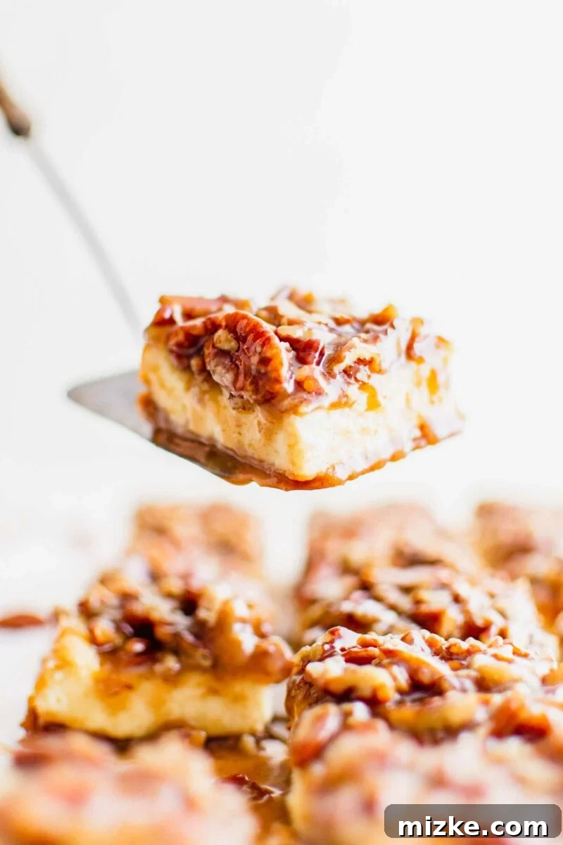 Decadent Pecan Pie Cheesecake Bars 4 A piece of pecan pie cheesecake bar is being carefully lifted from the baking dish, revealing its golden crust and creamy layers.