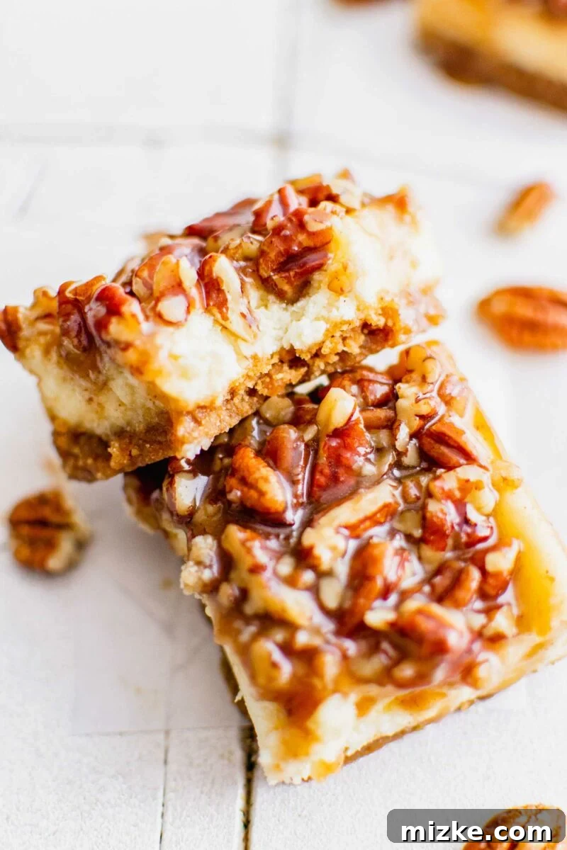 Decadent Pecan Pie Cheesecake Bars 7 Two perfectly cut pecan pie bars are elegantly placed next to each other on a clean white surface, showcasing their golden crust and luscious topping.