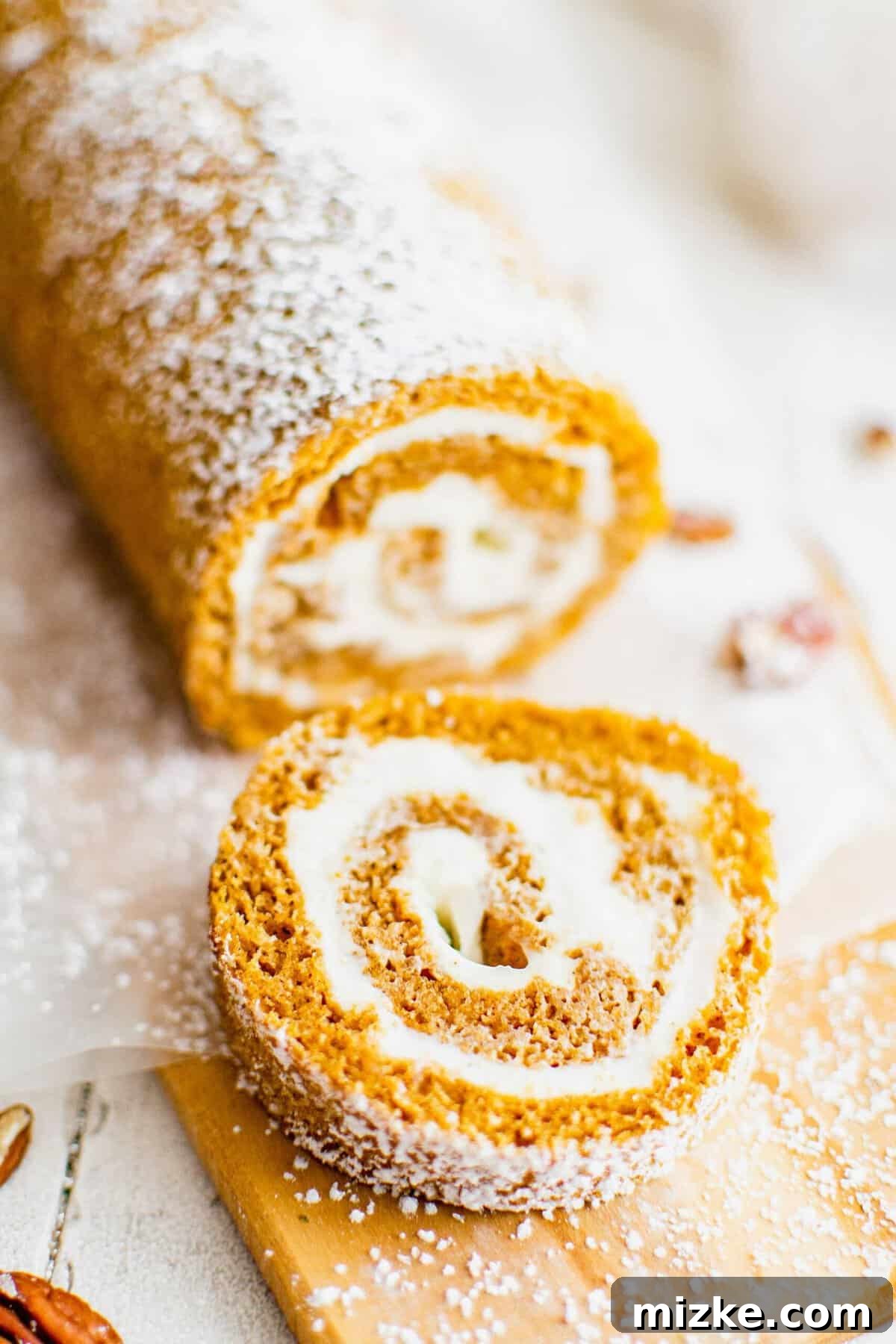Soft and spiced pumpkin roll with luscious cream cheese frosting, a perfect fall dessert. A perfectly sliced pumpkin roll on a rustic wooden cutting board, revealing the beautiful cream cheese frosting spiral.