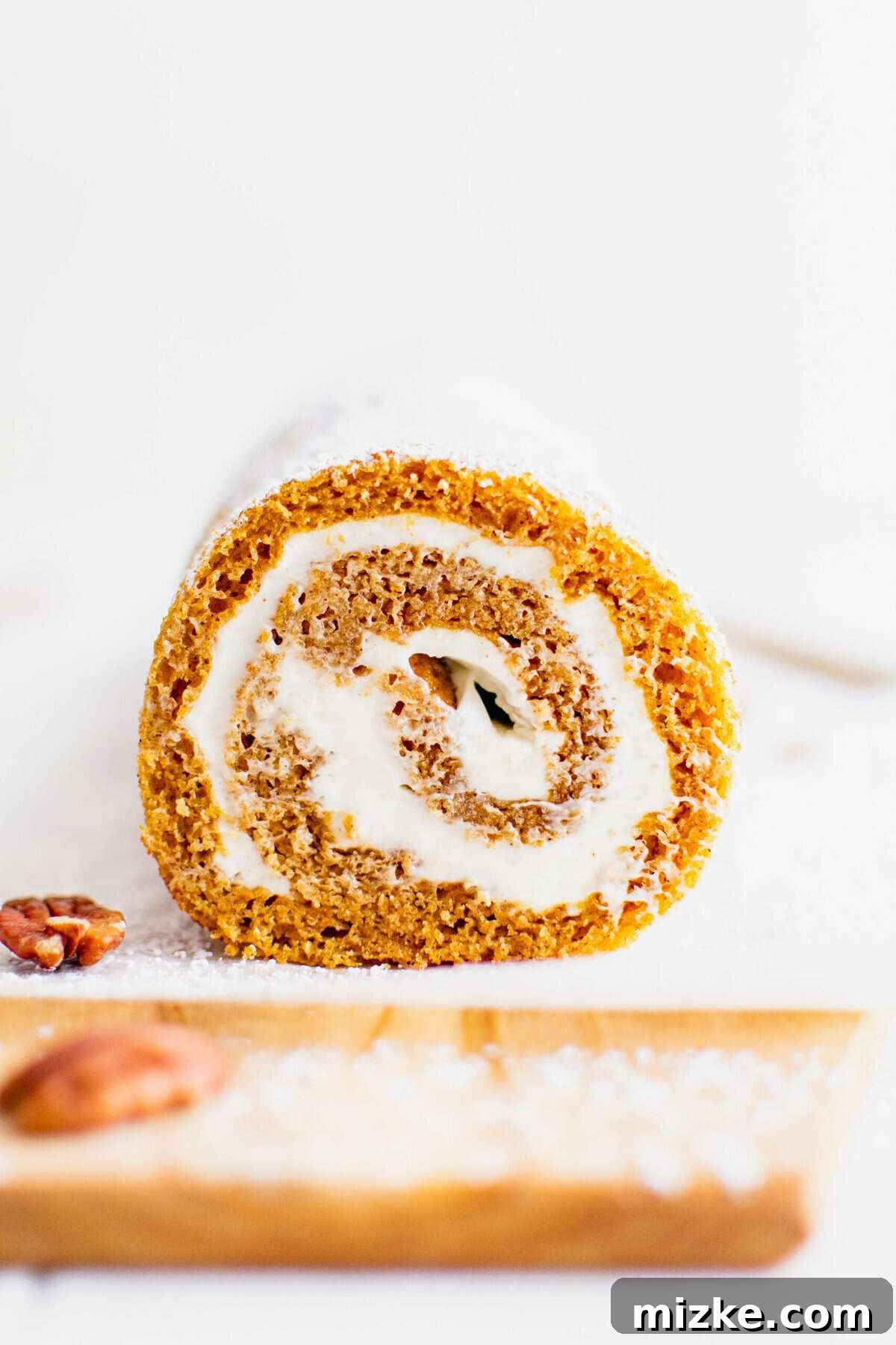 The perfect pumpkin cake ready to be rolled and filled. A freshly baked pumpkin roll, unadorned, resting on parchment paper on a wooden cutting board.