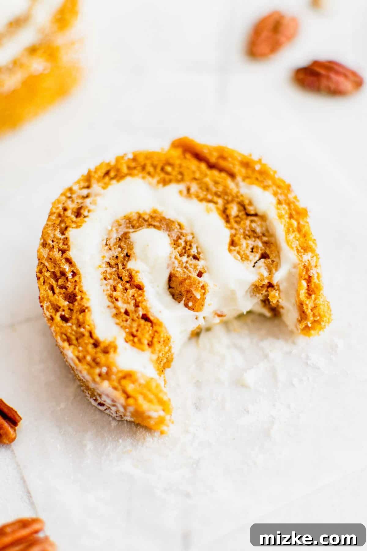 A tempting bite of spiced pumpkin roll with creamy filling. An overhead shot of a single slice of pumpkin roll with a bite taken out, resting on a white countertop.
