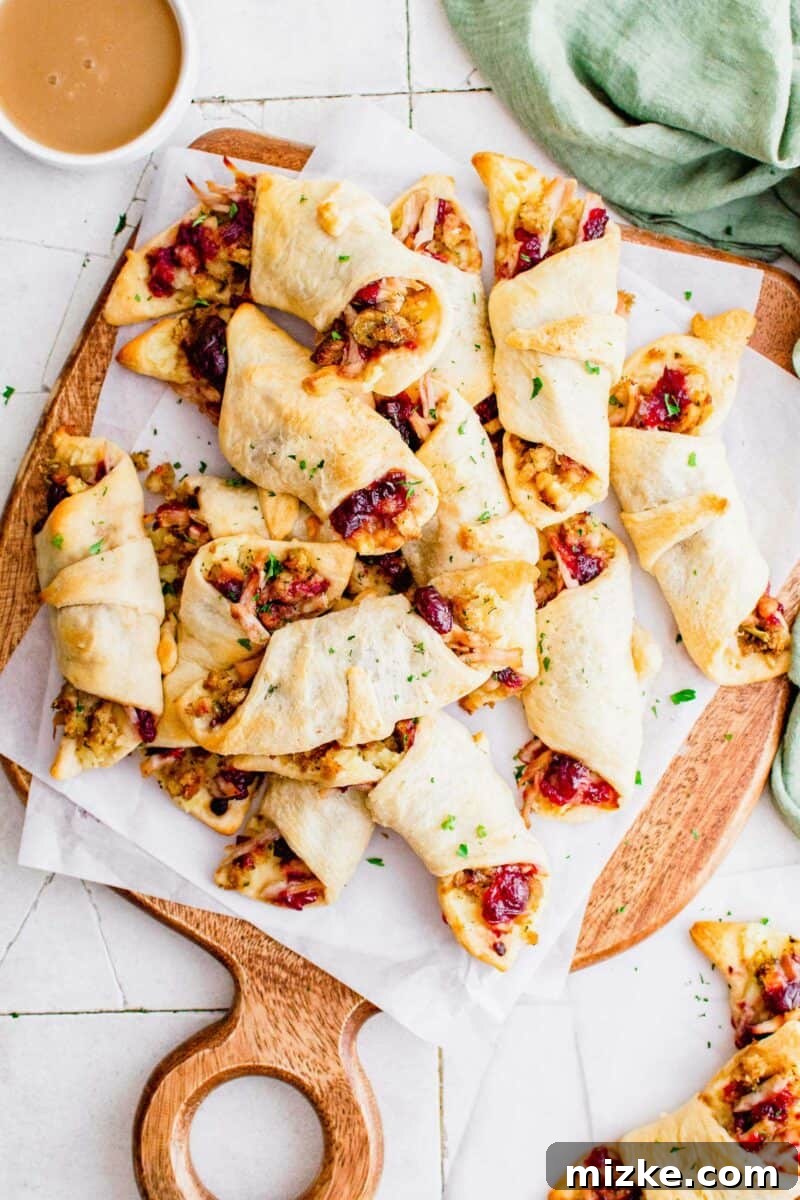 Holiday Feast Pockets 2 A large serving of rolled Thanksgiving appetizers are presented on a white parchment paper on a wooden surface.