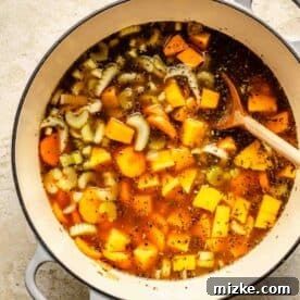 A wooden spoon is in the soup along with celery and carrots visible, simmering gently.