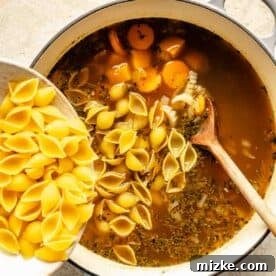 Dry pasta shells are being poured into the soup mixture.