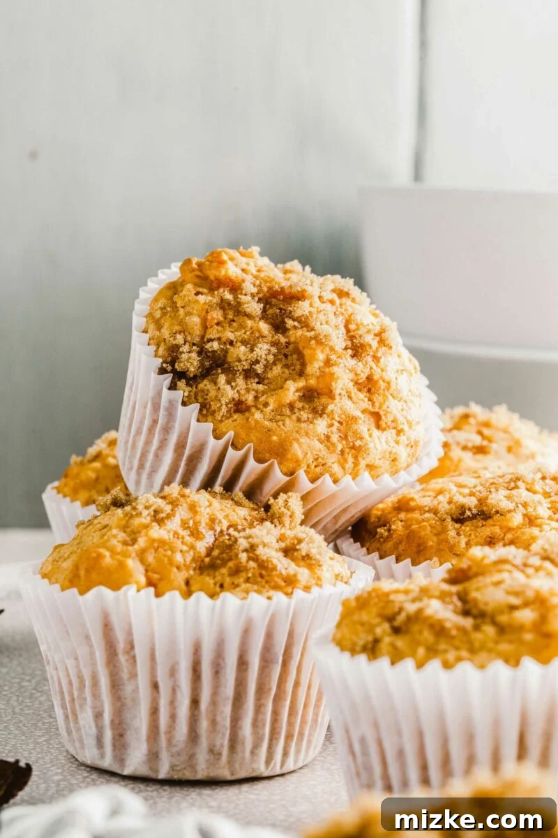 Golden Spiced Sweet Potato Muffins 5 A stack of golden-brown sweet potato muffins, with one muffin placed delicately on top of several others, creates an inviting visual on a pristine white surface.