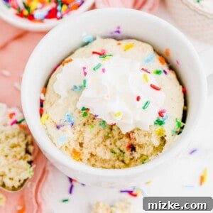 Funfetti mug cake topped with whipped cream and sprinkles, ready to eat