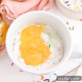 Applesauce and water with funfetti cake mix combined in a white mug