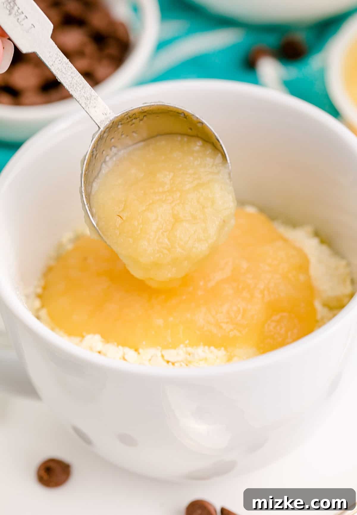 Instant Chocolate Chip Mug Treat 6 A tablespoon of applesauce being carefully added into a mug containing dry cake mix