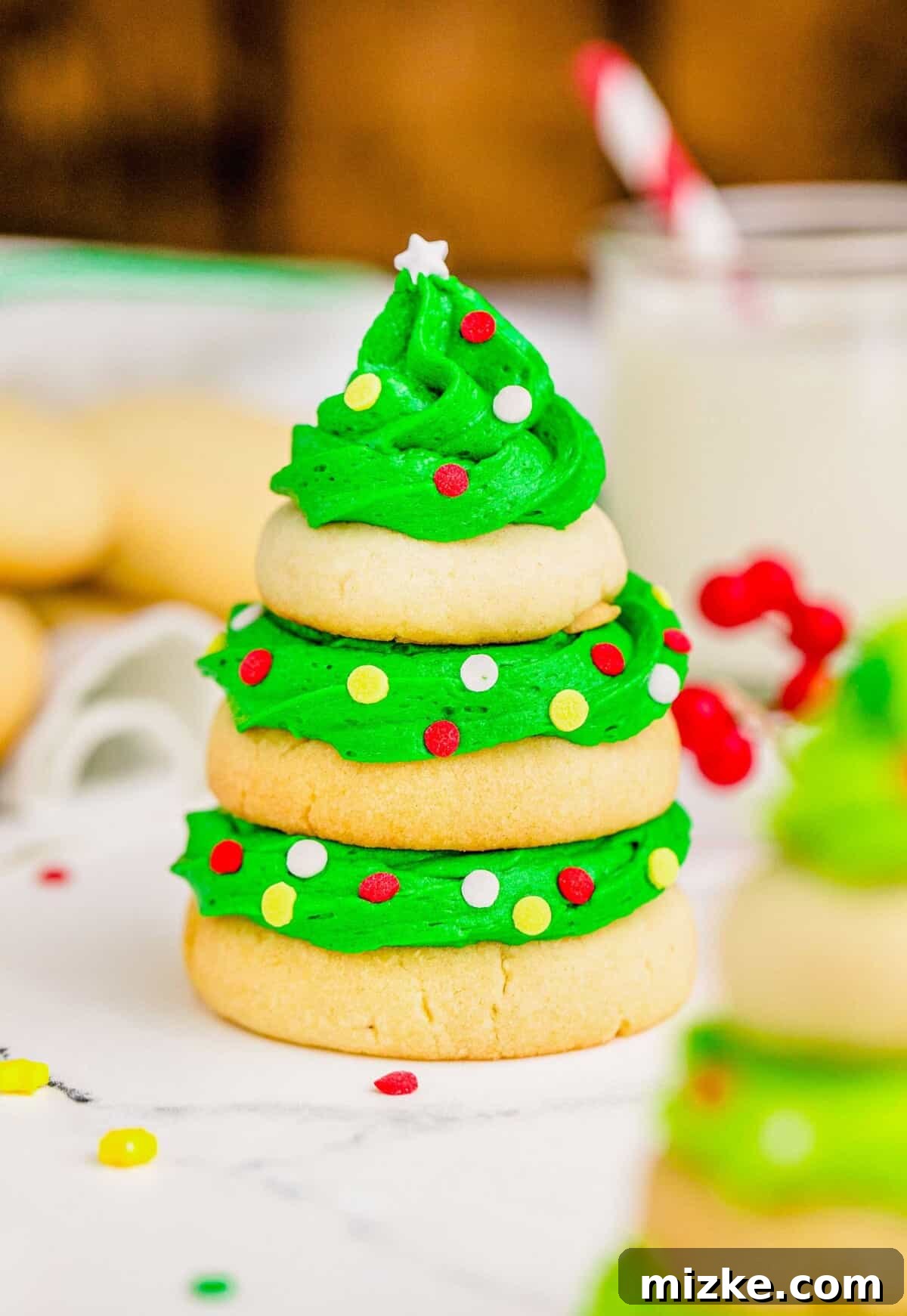Three sugar cookies are stacked with green icing and sprinkles to resemble a Christmas tree, presented on a festive plate.
