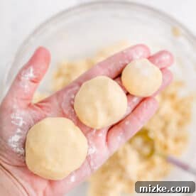 A hand is holding three distinct balls of cookie dough, ready for baking.