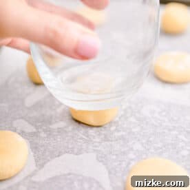 Cookie dough balls being pressed with a glass on a baking sheet.