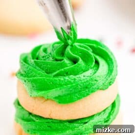 Green icing being piped onto sugar cookies in a stack, creating a delightful Christmas tree.