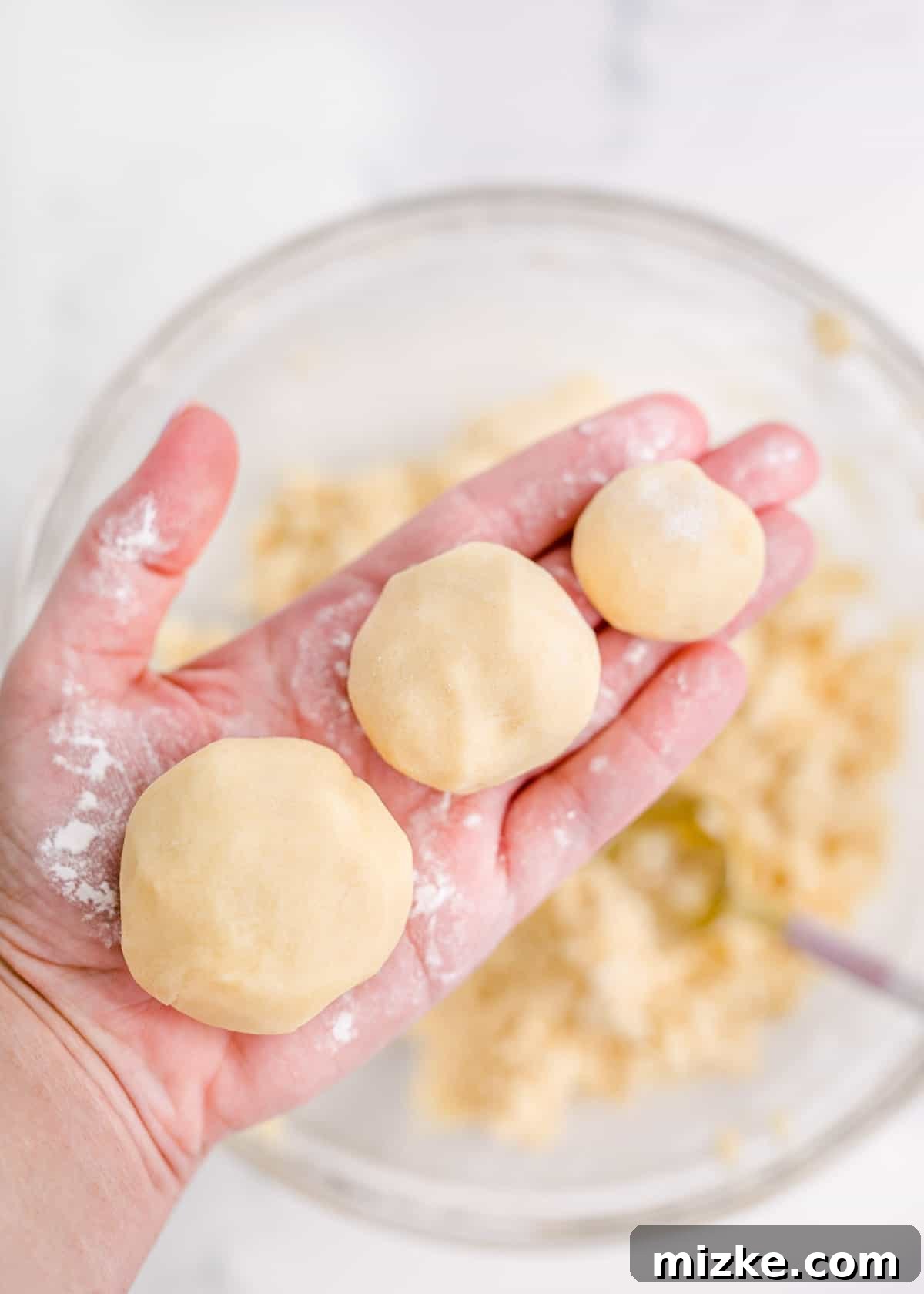 A hand is holding three distinct balls of cookie dough, showcasing different sizes for the stacked tree effect.