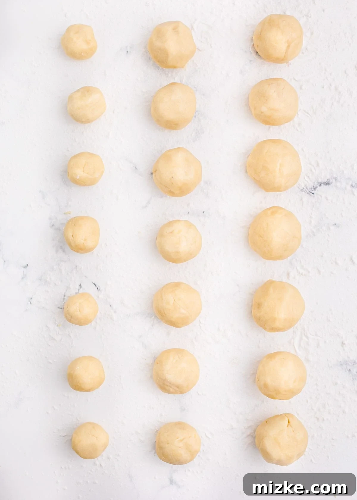 Balls of cookie dough in three different sizes are neatly arranged on a counter before flattening.
