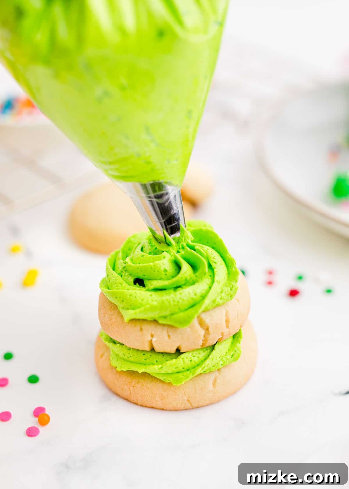 Vibrant green icing is being piped onto a stack of sugar cookies to form a festive Christmas tree shape.