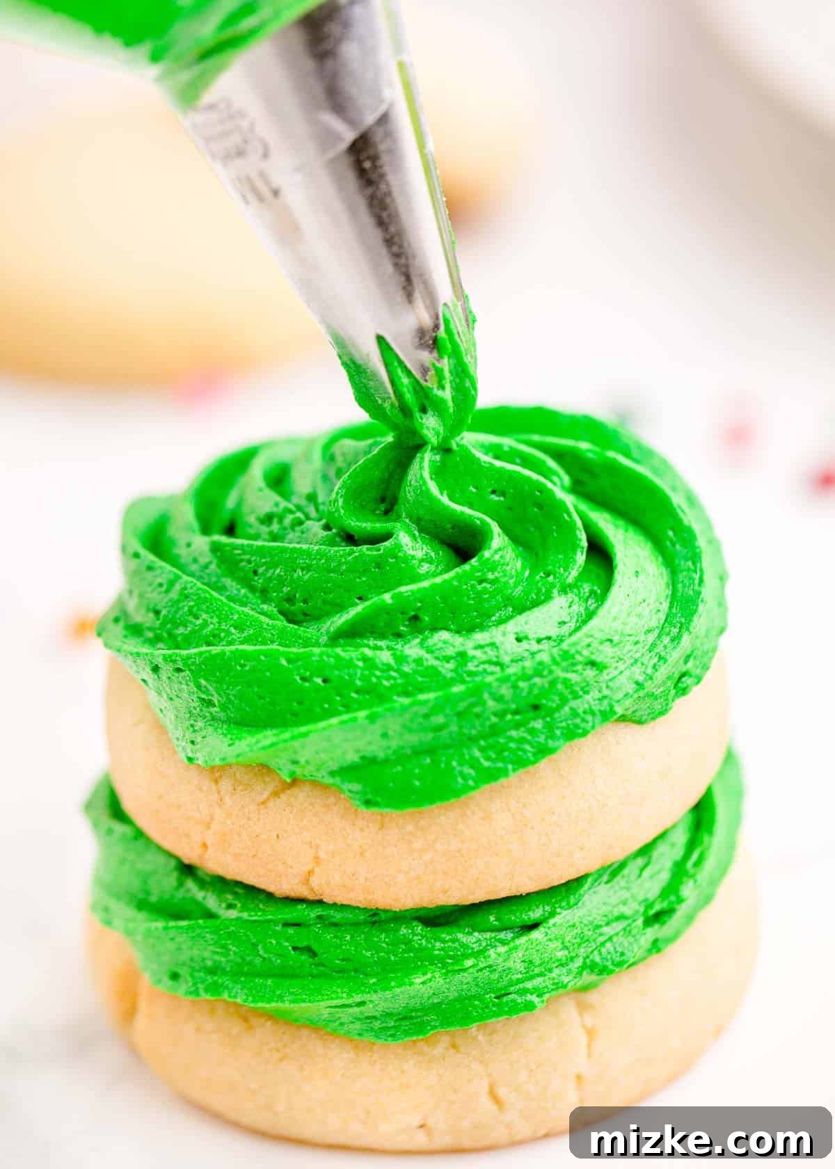 Green icing is being expertly piped onto sugar cookies arranged in a stack, building the tree structure.