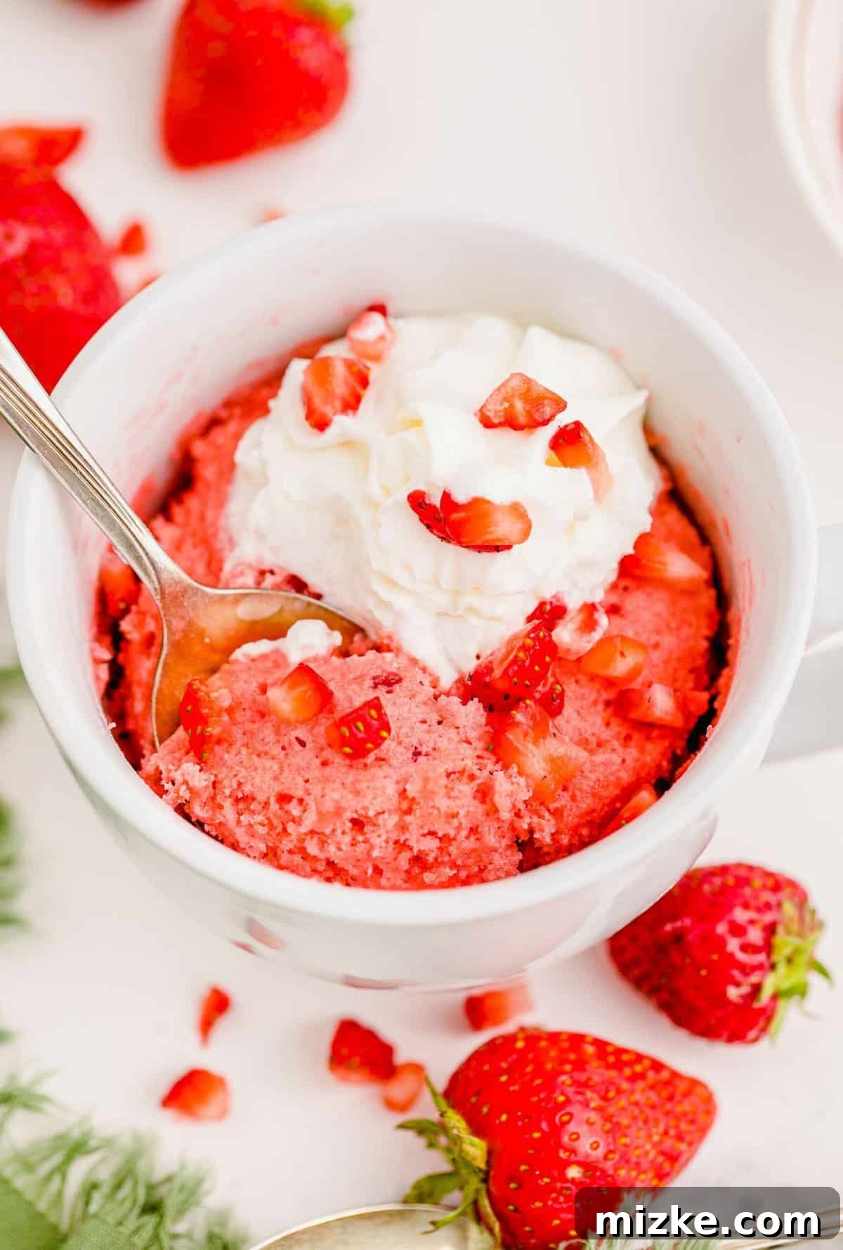 Spoon digging into strawberry mug cake topped with luscious whipped cream