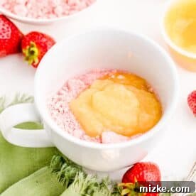 Applesauce added on top of strawberry cake mix in a white mug, ready for mixing