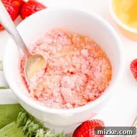 A metal spoon mixing strawberry cake mix and applesauce in a white mug