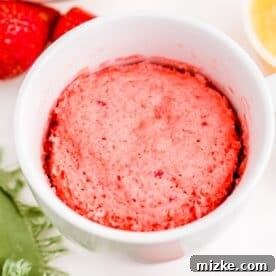 A freshly cooked strawberry mug cake in a white mug, fluffy and golden