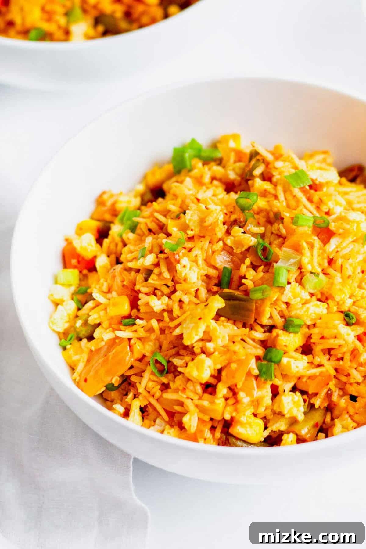 Kimchi fried rice in white bowl, garnished with thinly sliced green onions and a sprinkle of sesame seeds