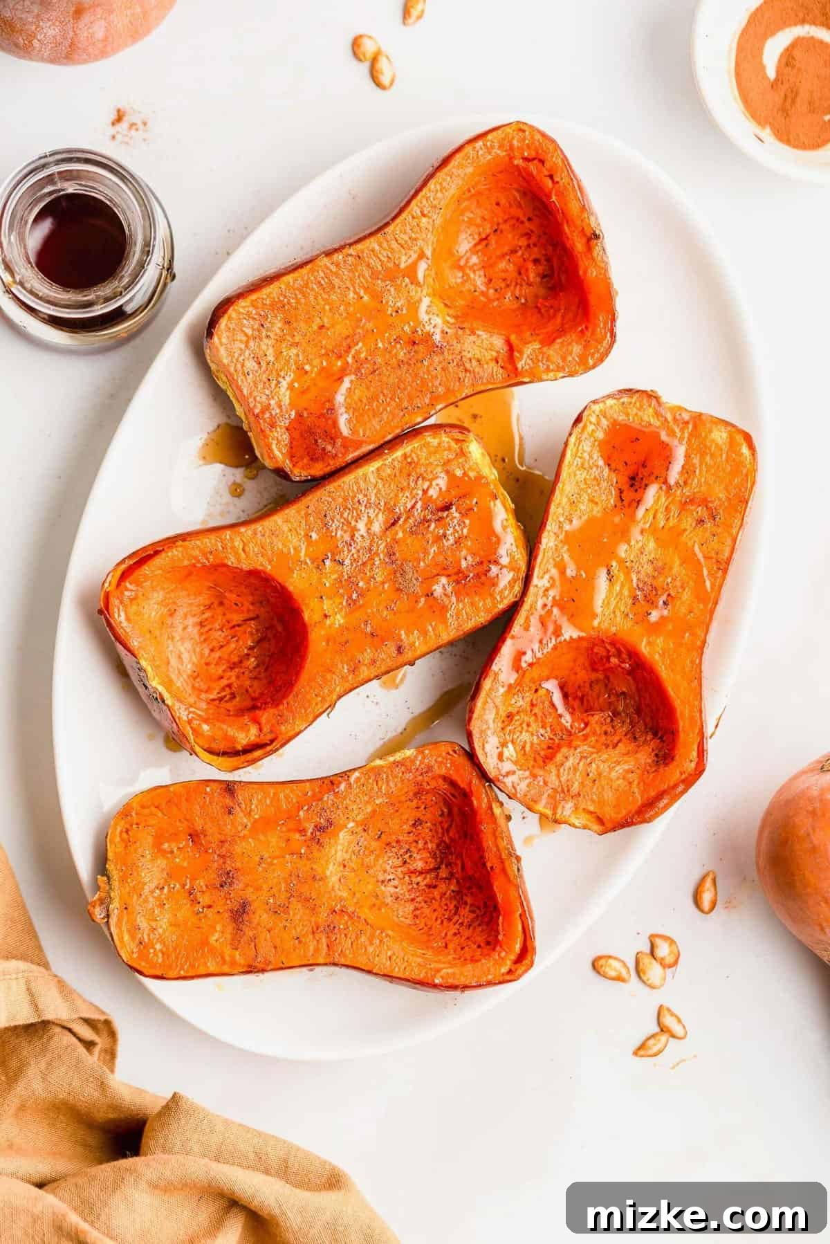 Caramelized Honeynut Squash 2 Golden roasted honeynut squash halves glistening with maple syrup and cinnamon, served attractively on a white platter, ready to be enjoyed.