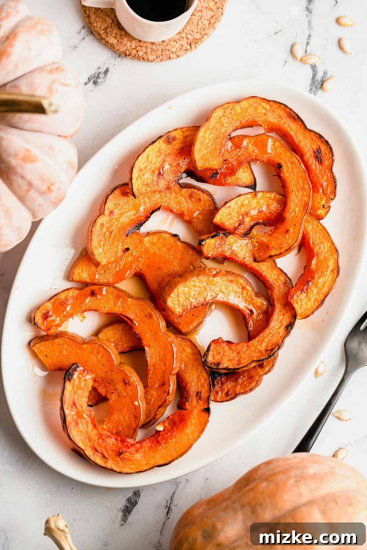 Golden Roasted Koginut Squash 2 Overhead view of perfectly roasted koginut squash slices arranged on a pristine white serving platter, glistening with maple syrup.