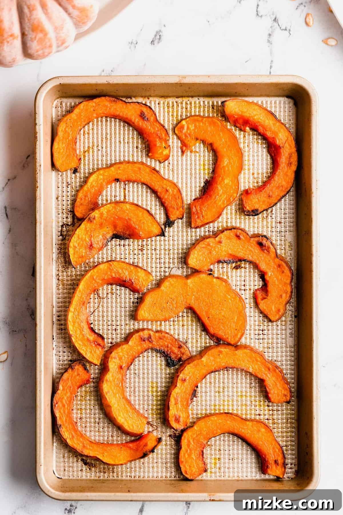 Golden Roasted Koginut Squash 5 Overhead view of glistening roasted koginut squash slices perfectly browned on a baking sheet, fresh out of the oven.