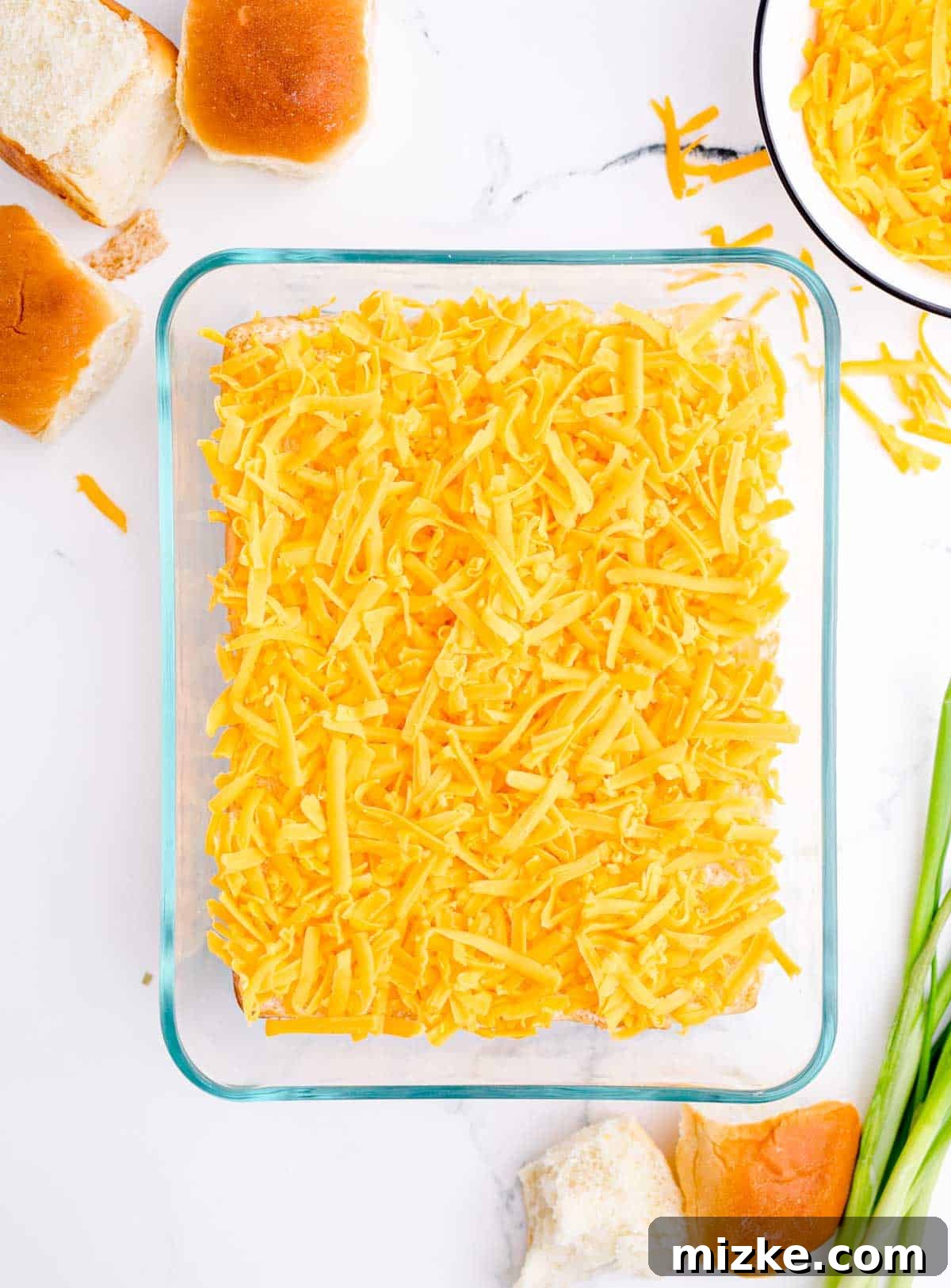 Morning Bites 11 A base layer of shredded cheddar cheese spread evenly over the bottom halves of dinner rolls in a glass baking dish